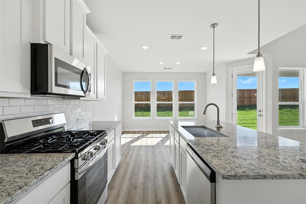 2515 Ridgecrest Lane Sherman, TX 75092 - Photo 5 of 40 Kitchen featuring stainless steel appliances, white cabinetry, a center island with sink, light wood-style floors, and light stone countertops