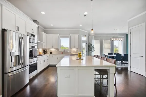 a kitchen with stainless steel appliances granite countertop a refrigerator a sink dishwasher a stove and white cabinets with wooden floor