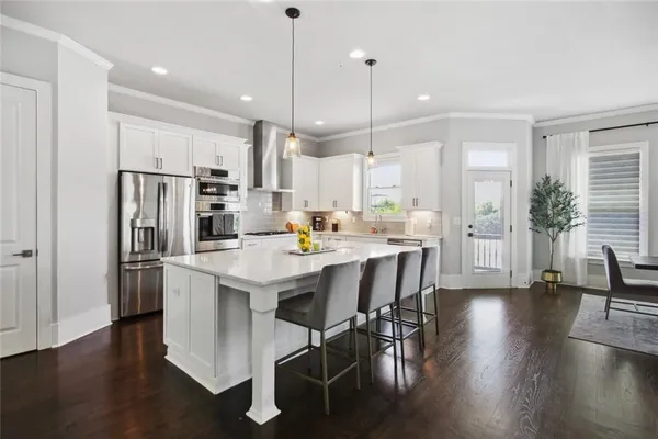 a kitchen with stainless steel appliances granite countertop a refrigerator a stove a sink a dining table and chairs with wooden floor