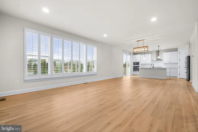 a view of empty room with wooden floor and kitchen view
