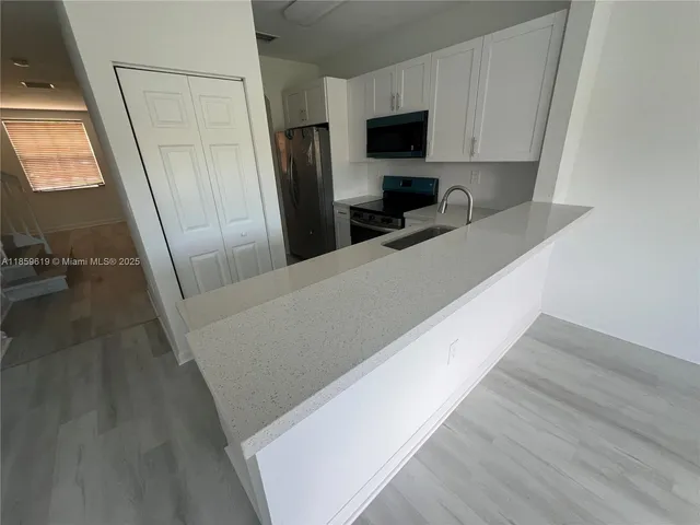 a living room with stainless steel appliances a refrigerator a couch a flat screen tv and a fireplace