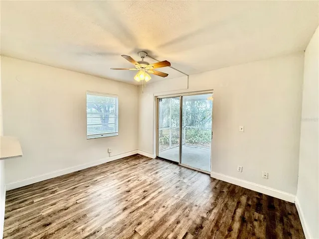 an empty room with wooden floor fan and windows