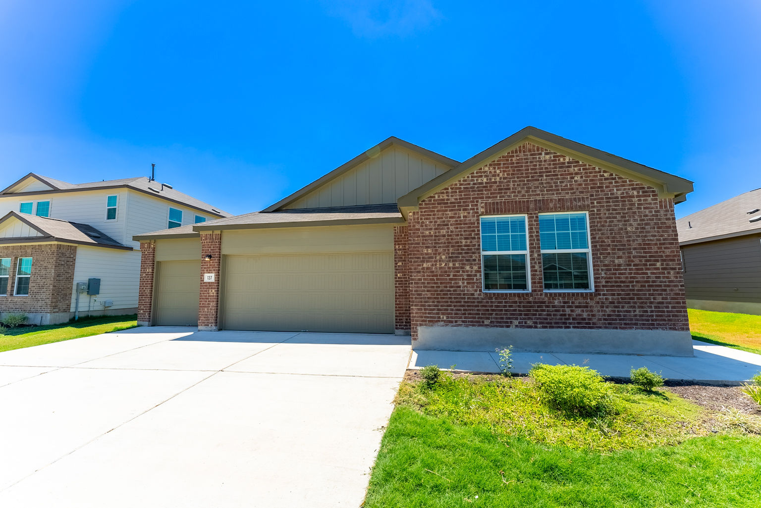 137 River Rise Road Kyle, TX 78640 - Photo 2 of 26 View of front of property featuring driveway, a garage, brick siding, board and batten siding, and a front lawn