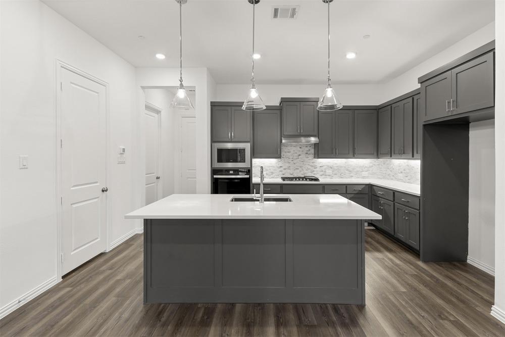 1237 Doris May Drive Allen, TX 75013 - Photo 8 of 19 Modern kitchen featuring a central island with a sink, white countertops, gray cabinetry, stainless steel appliances, and wood-finish flooring