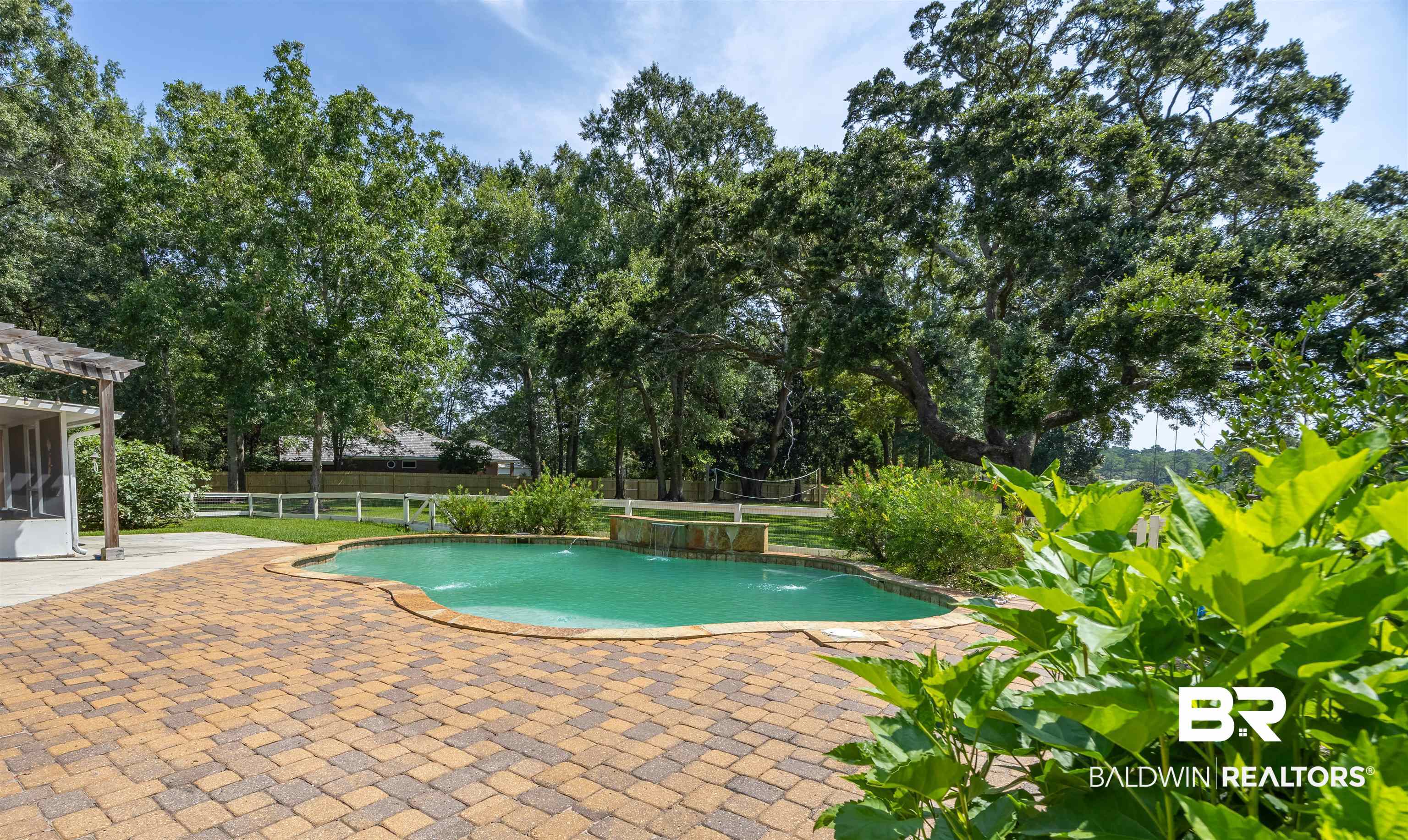 13677 Rebel Road Coden, AL 36523 - Photo 43 of 61 Resort-style pool area featuring a freeform swimming pool with water features, extensive paver patio, a shaded pergola, and abundant mature trees
