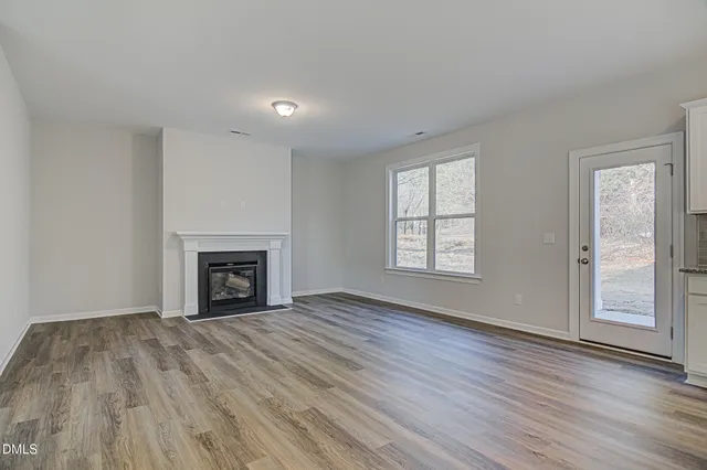 a view of an empty room with wooden floor fireplace and a window