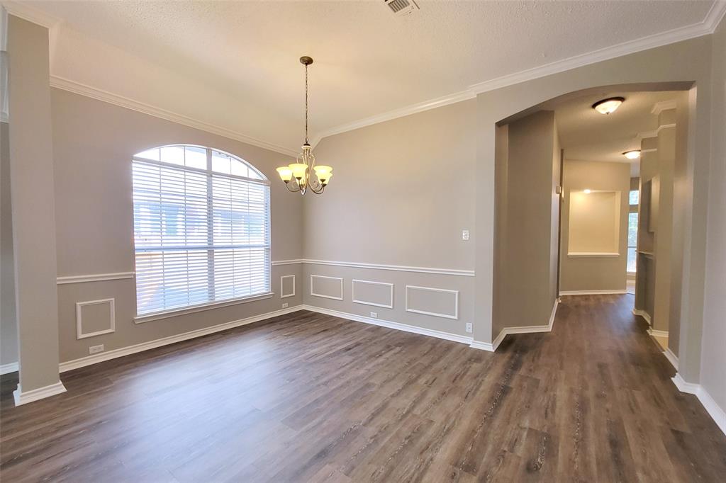 1604 Knoll Ridge Circle Corinth, TX 76210 - Photo 9 of 37 Spacious room featuring wood-finish flooring, a large arched window with blinds, decorative wainscoting, crown molding, and a chandelier