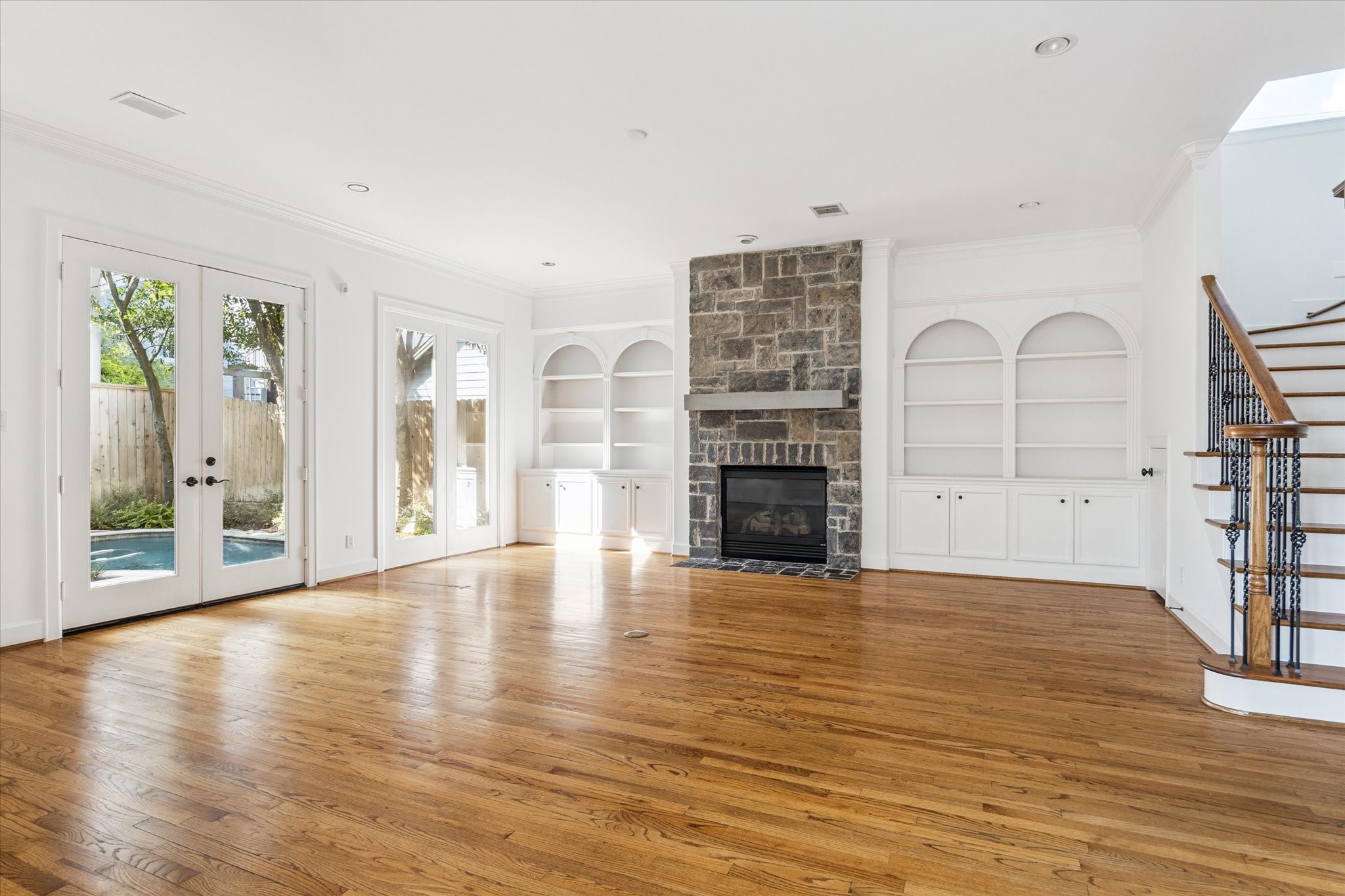 6106 Fordham Street Houston, TX 77005 - Photo 12 of 33 Spacious family room anchored by a striking floor-to-ceiling stone fireplace flanked by custom built-in cabinetry. Double French doors open to the backyard and pool, filling the room with natural light and a seamless indoor-outdoor connection.