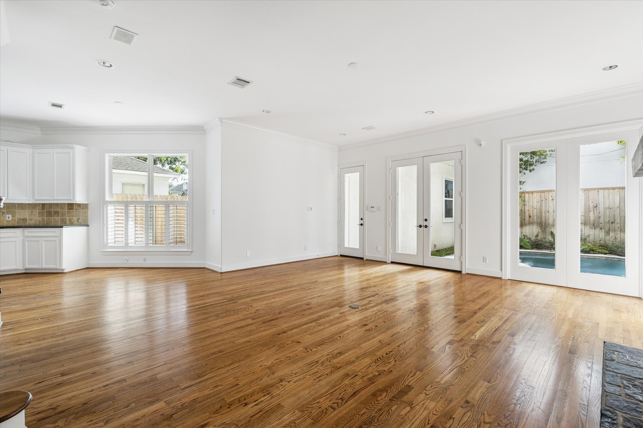 6106 Fordham Street Houston, TX 77005 - Photo 13 of 33 An open-concept living and kitchen space with expansive windows and French doors overlooking the pool. The layout provides effortless flow for everyday living and entertaining, complemented by hardwood floors and crisp white finishes.