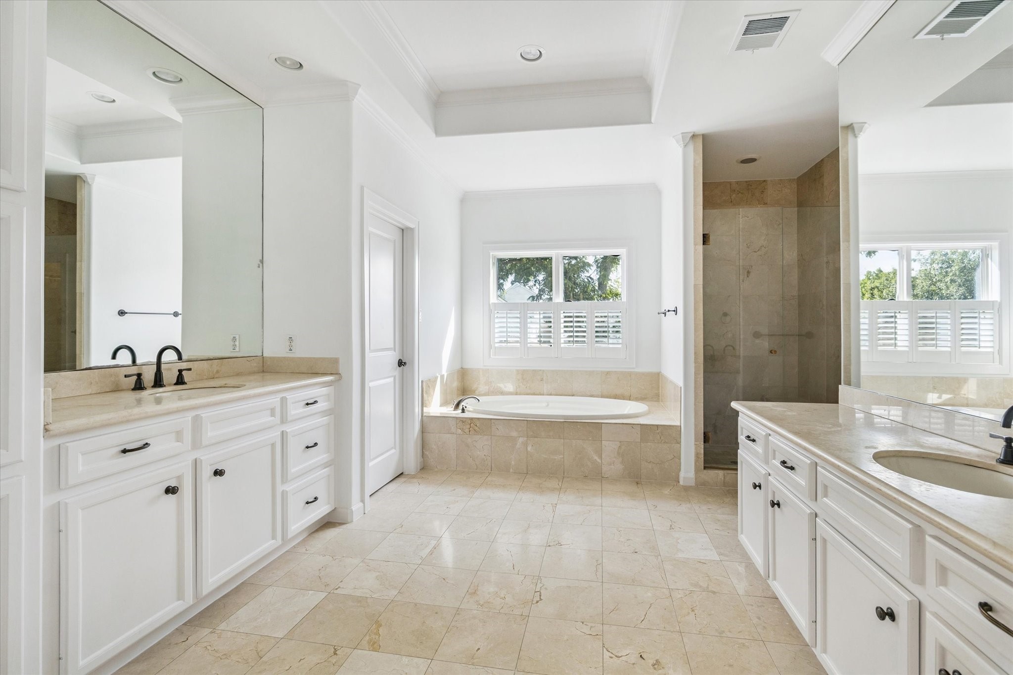 6106 Fordham Street Houston, TX 77005 - Photo 17 of 33 Light-filled primary bath with dual vanities, marble floors, soaking tub beneath a picture window, and a glass-enclosed shower. Classic design and ample storage combine beauty with functionality.