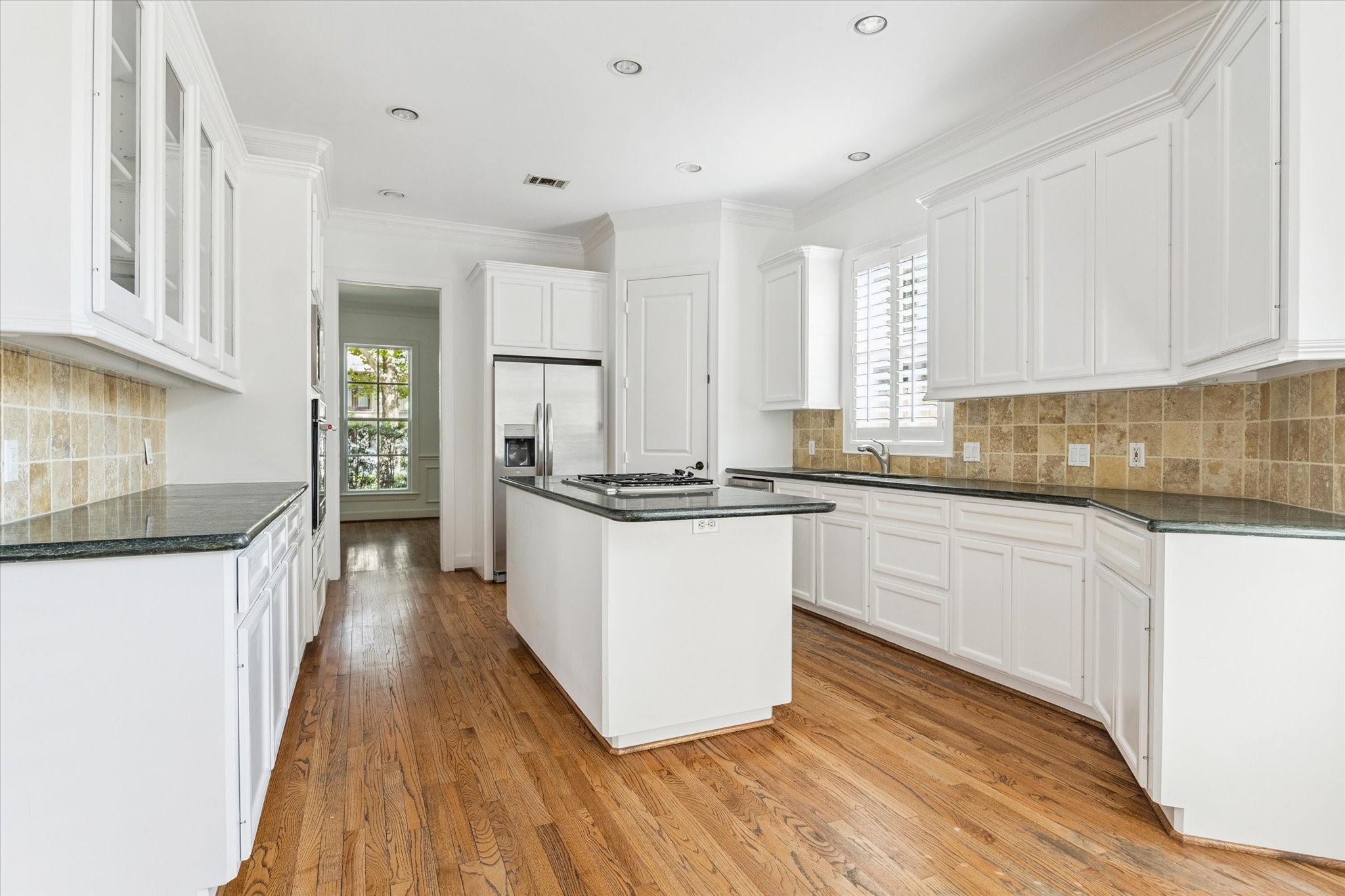 6106 Fordham Street Houston, TX 77005 - Photo 7 of 33 Bright and functional kitchen design featuring display cabinetry, stone backsplash, and hardwood floors extending throughout the main level.