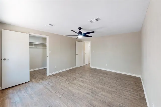 a view of an empty room with wooden floor and a ceiling fan