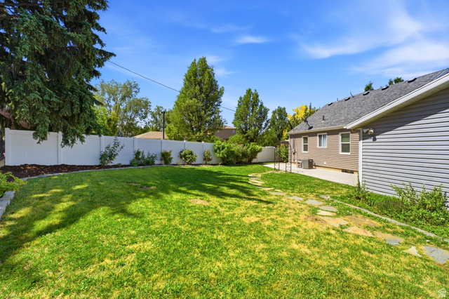 1925 South Main Street Bountiful, UT 84010 - Photo 32 of 48 Expansive lawn area featuring a white privacy fence, established trees, a concrete patio, and a stone-paver walkway