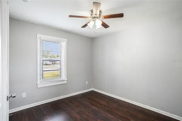 an empty room with wooden floor chandelier fan and windows