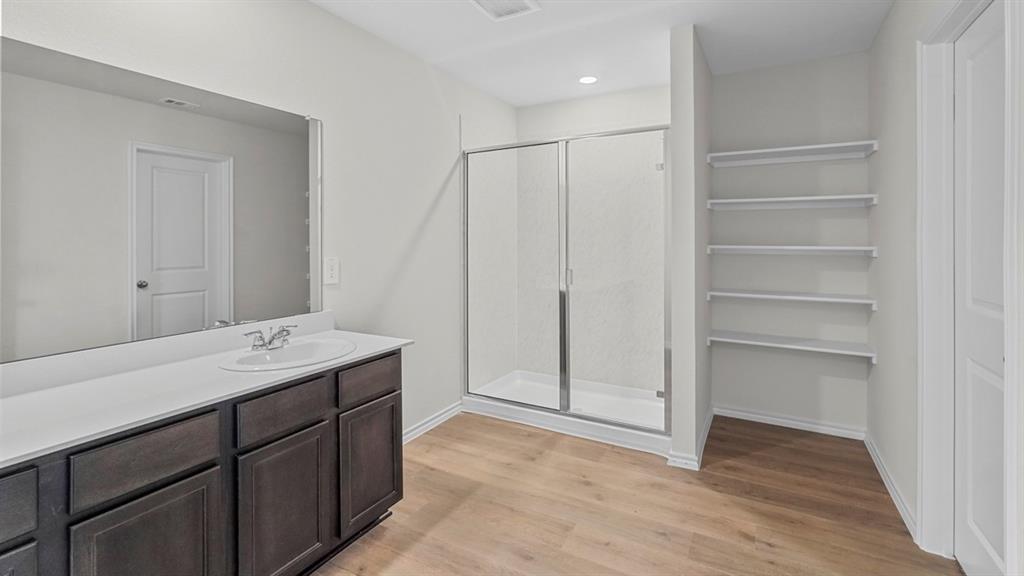 1953 Freeman Street Tyler, TX 75704 - Photo 18 of 32 Bathroom featuring a spacious vanity with dark wood-finish cabinetry and a white countertop, a large built-in mirror, a glass-enclosed shower, and wood-finish flooring