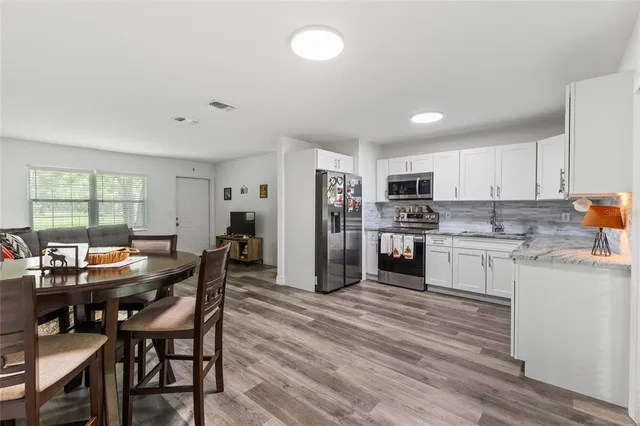 a kitchen with stainless steel appliances kitchen island granite countertop a dining table chairs and refrigerator