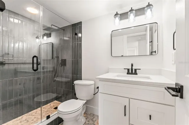 a bathroom with a toilet sink vanity granite and shower