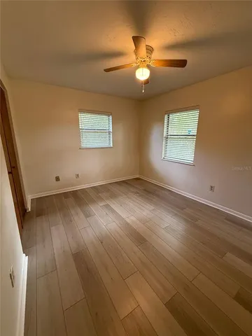 an empty room with wooden floor fan and window