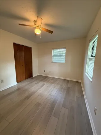 an empty room with wooden floor chandelier fan and windows