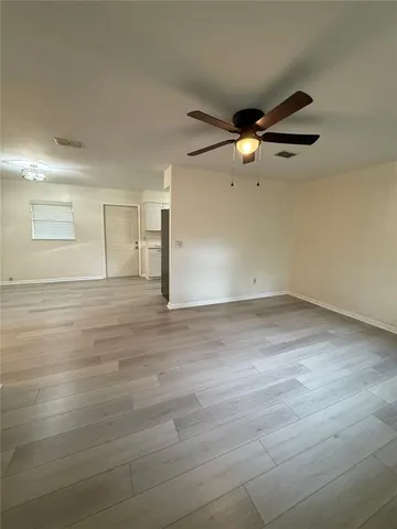 an empty room with wooden floor ceiling fan and windows