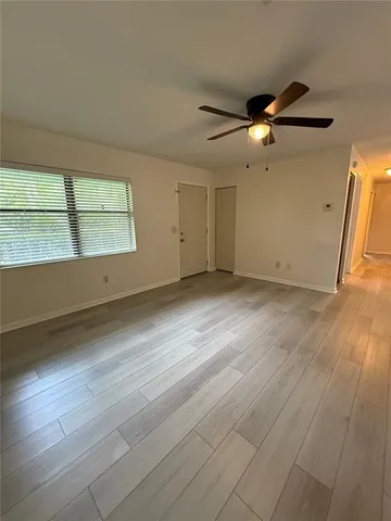 an empty room with wooden floor fan and windows