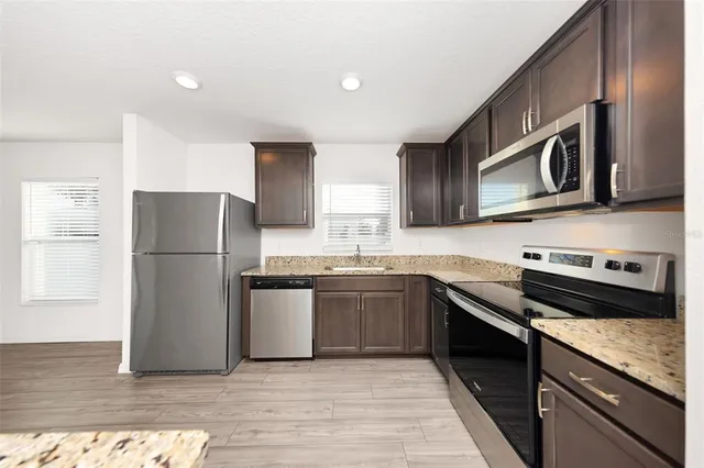 a kitchen with stainless steel appliances granite countertop a refrigerator a stove top oven a sink and dishwasher with wooden floor