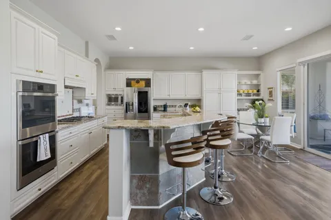 a kitchen with stainless steel appliances granite countertop a stove top oven a sink a dining table and chairs with wooden floor