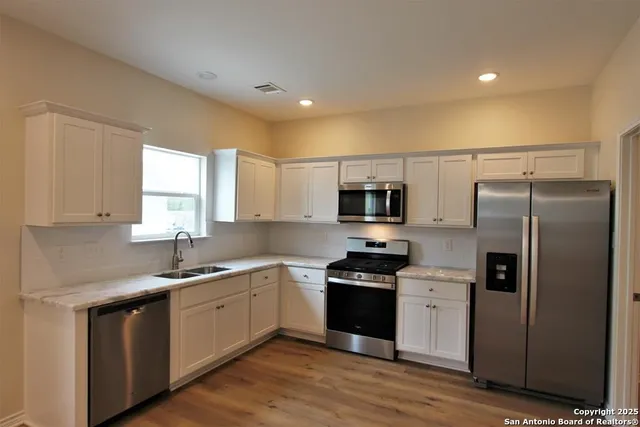 a kitchen with stainless steel appliances granite countertop a sink a stove a refrigerator cabinets and a window