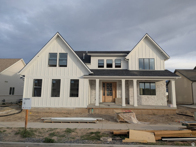 Modern farmhouse exterior featuring white board and batten siding, light-colored stone accents, a dark shingle roof, black-framed windows, and a covered porch with white columns
