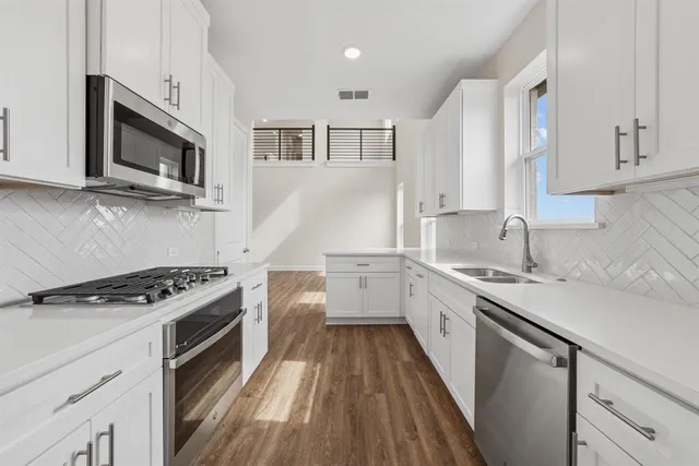 a kitchen with stainless steel appliances a sink dishwasher stove microwave and cabinets with wooden floor