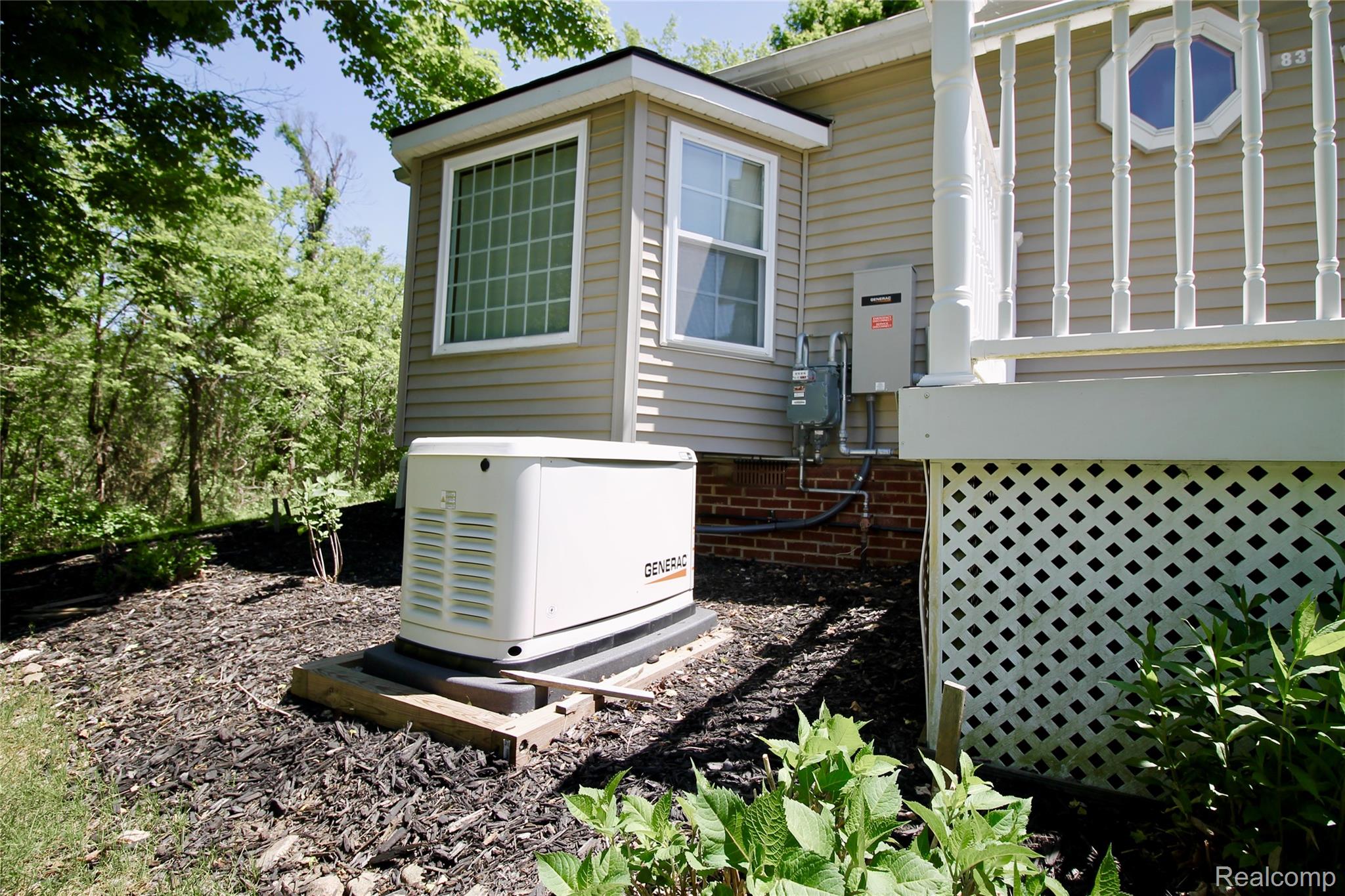 8372 Parshallville Road Fenton, MI 48430 - Photo 36 of 44 Property exterior featuring a whole-house generator, tan siding, multiple windows, a decorative octagonal window, and a white lattice foundation skirt