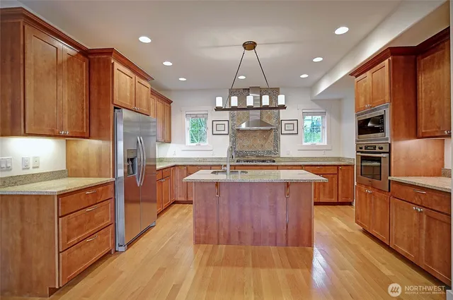 a large kitchen with stainless steel appliances a large counter top a stove a sink dishwasher a refrigerator and wooden cabinets with wooden floor