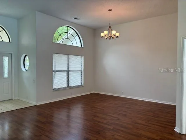 an empty room with wooden floor chandelier and windows