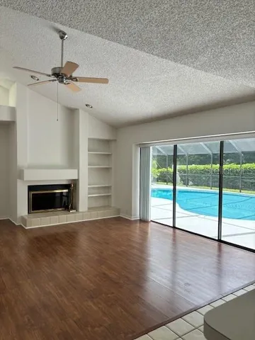 a view of an empty room with wooden floor fireplace and a window