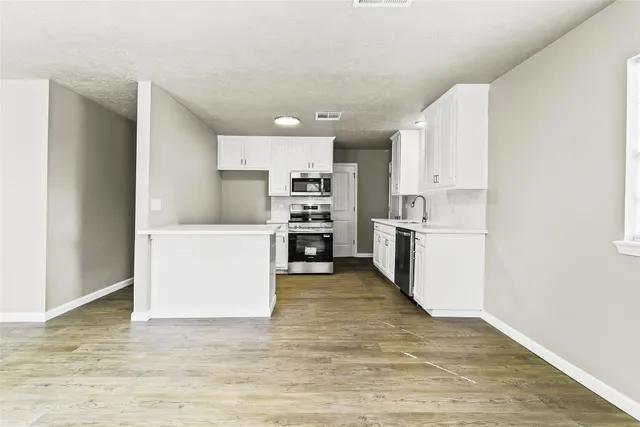 a kitchen with kitchen island a stove a sink a refrigerator white cabinets and wooden floor