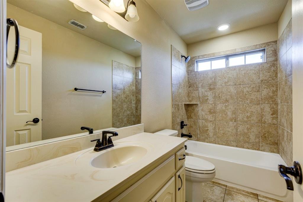 1522 Blue Jay Road Garland, TX 75043 - Photo 31 of 32 Bathroom featuring a single vanity with an integrated sink, oil-rubbed bronze fixtures, a framed mirror, a built-in tub with tile surround, and a high-set window
