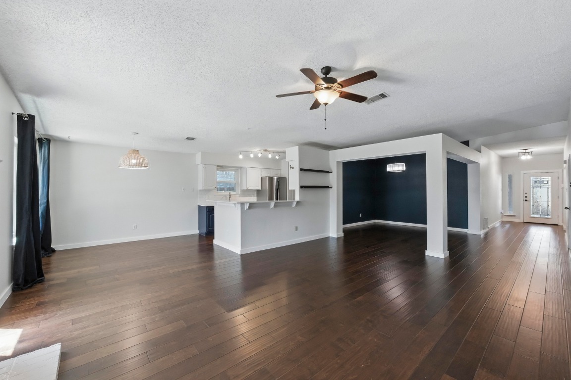 a view of an empty room with wooden floor and a kitchen