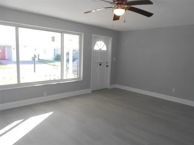 an empty room with wooden floor fan and windows