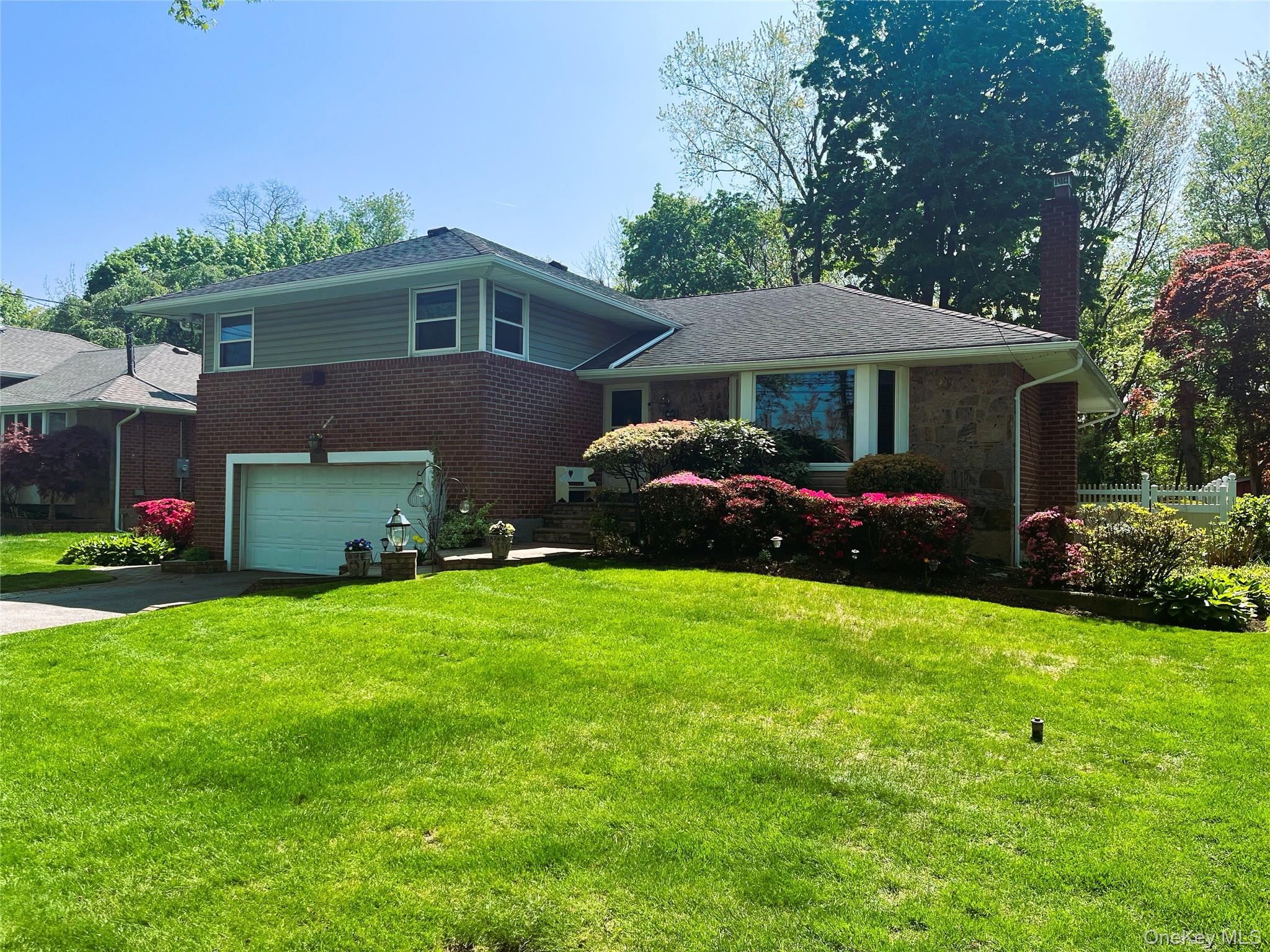 Tri-level home featuring a front yard, driveway, a chimney, brick siding, and a garage