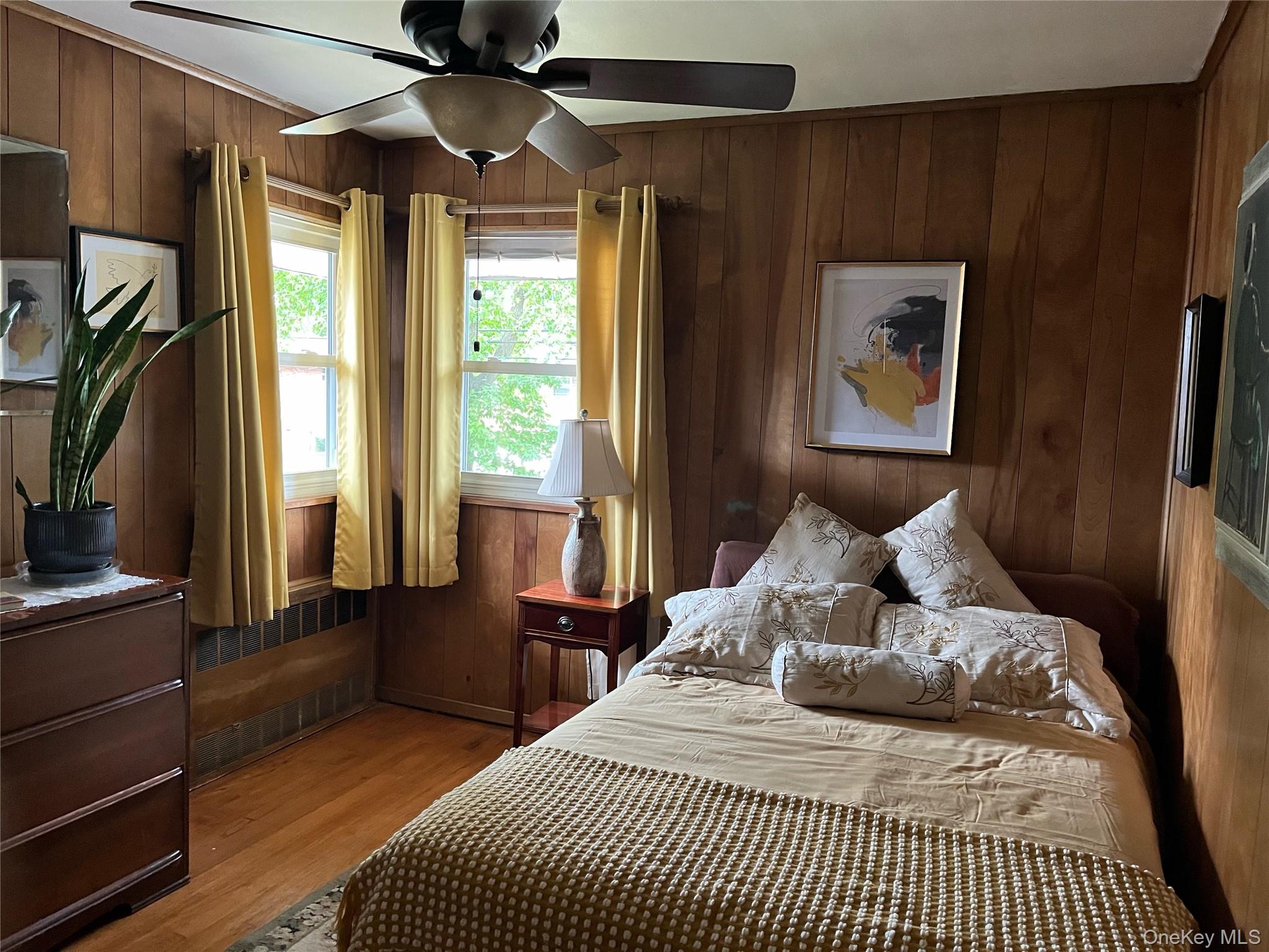 24 Cedar Road Westbury, NY 11590 - Photo 11 of 21 Bedroom 2 featuring wood walls, light wood-style flooring, radiator, and a ceiling fan