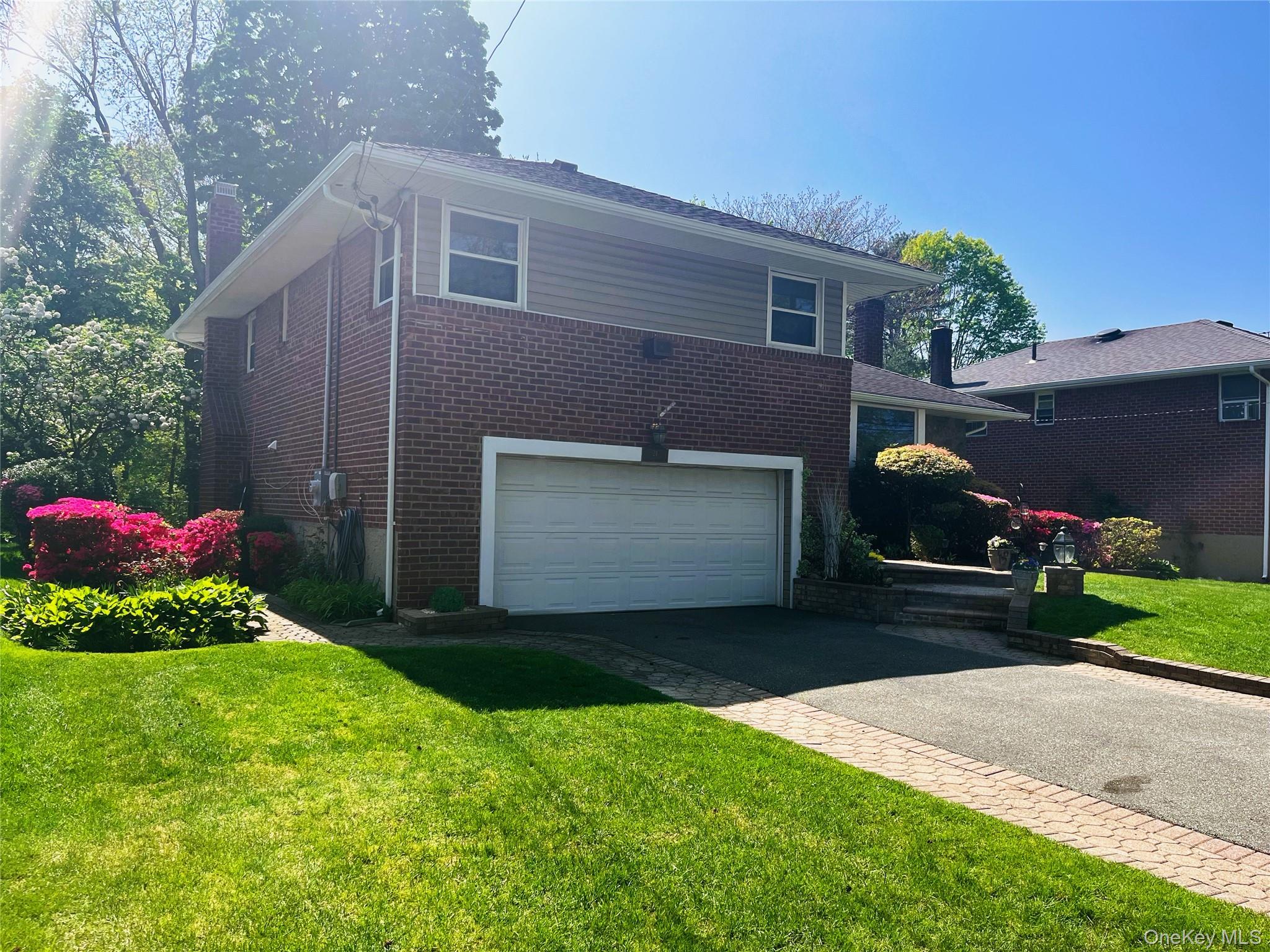24 Cedar Road Westbury, NY 11590 - Photo 2 of 21 View of side of home featuring asphalt driveway, brick siding, a yard, an attached garage, and a chimney