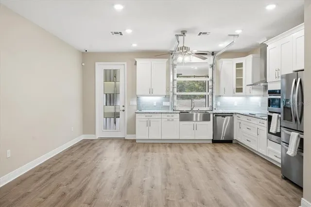 a kitchen with stainless steel appliances granite countertop a refrigerator a sink dishwasher a oven and white cabinets with wooden floor