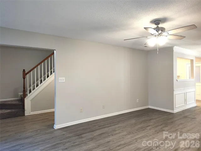 a view of an empty room with wooden floor and a chandelier fan