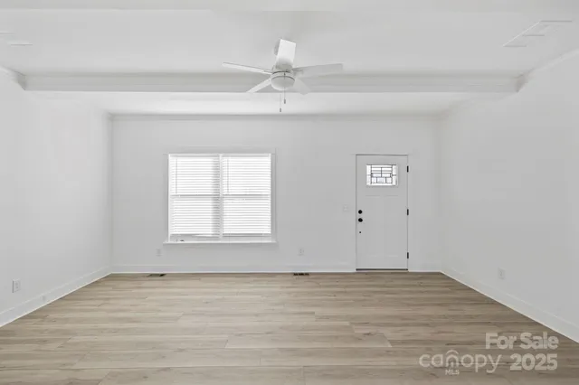 an empty room with wooden floor fan and window