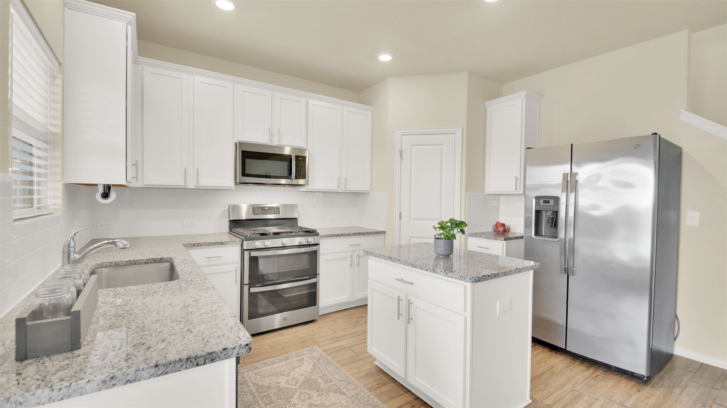 13716 Sugar Bush Path Manor, TX 78653 - Photo 24 of 37 Kitchen featuring white cabinetry, stainless steel appliances, a kitchen island, light stone countertops, and light wood-style floors