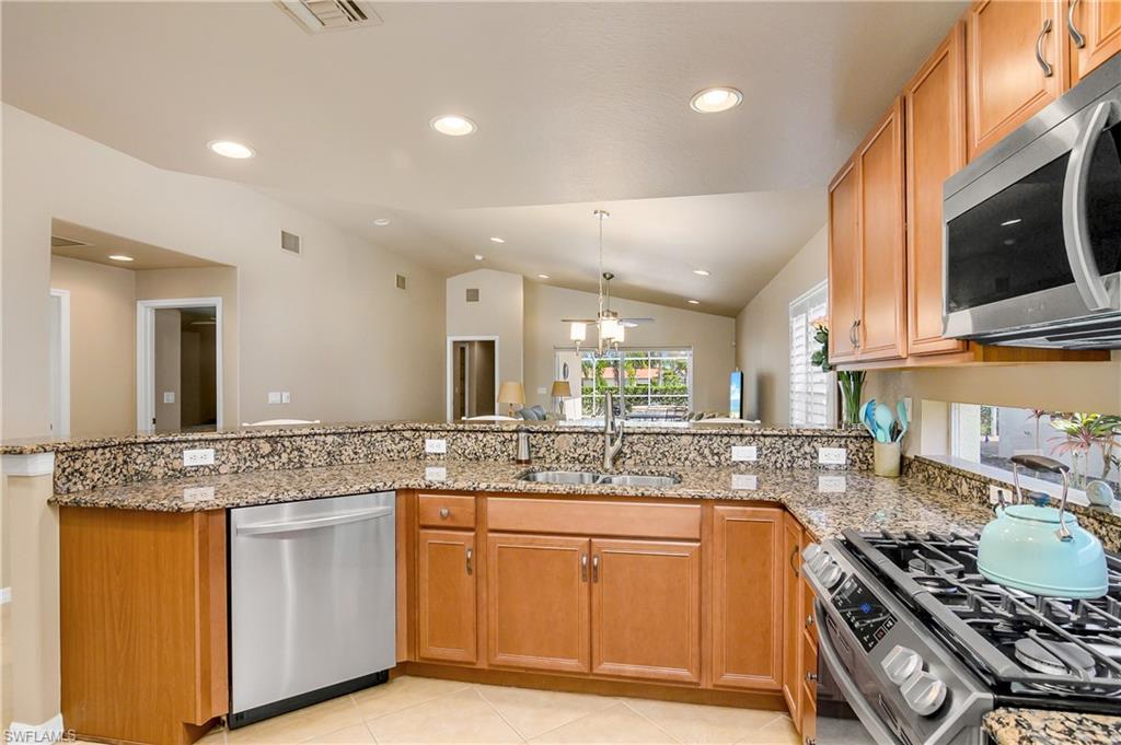 19633 Villa Rosa Loop Estero, FL 33967 - Photo 10 of 50 Kitchen with vaulted ceiling, light stone countertops, stainless steel appliances, sink, and kitchen peninsula