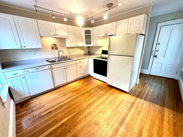 a kitchen with granite countertop a refrigerator a sink dishwasher a stove top oven a washer and dryer with wooden floor