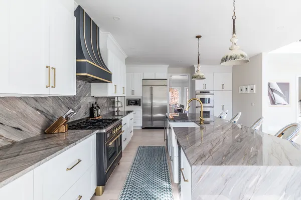 a large kitchen with stainless steel appliances granite countertop a stove a sink dishwasher a refrigerator and white cabinets with wooden floor