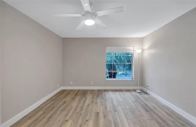 an empty room with wooden floor chandelier fan and windows