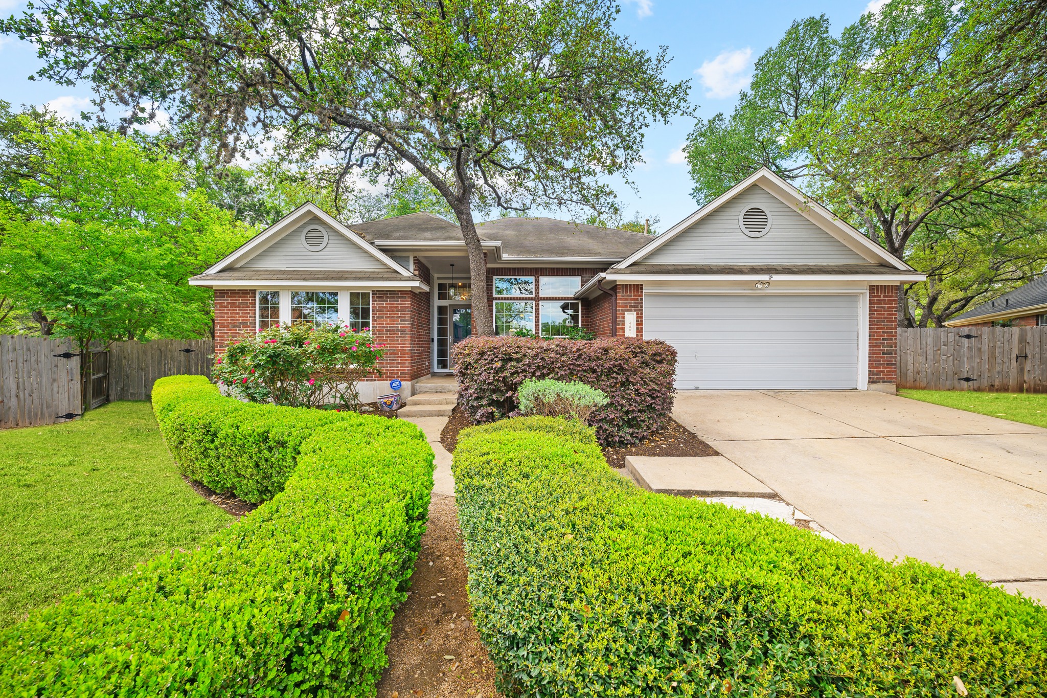 Ranch-style house with brick siding, a garage, driveway, a shingled roof with partial gutters and mature landscaping